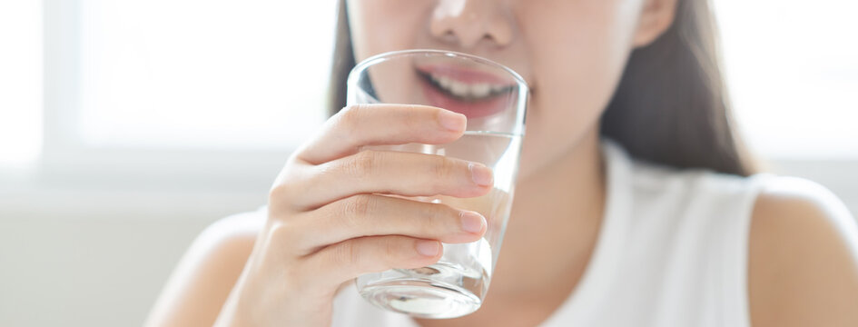 Happy beautiful, asian young woman, girl drinking, sip fresh glass of water for hydration of body, holding transparent glass in her hand, thirsty at home. Health care, healthy lifestyle concept.
