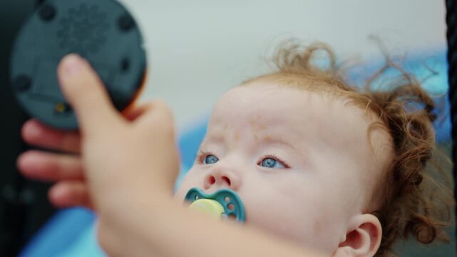 Baby girl with a baboo pacifier looking up at a button toy held above her by a therapist hand.