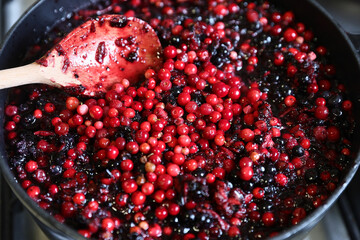 Traditional home-cooked lingonberry and forest blueberry jam cooking in a pot with a wooden spoon. © Silviu