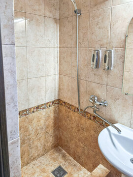 Tiled bathroom shower with handheld fixture and wall dispensers. Compact shower area with basin and textile curtain. Bathroom renovation and interior design. Domestic hygiene and daily washing