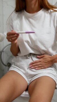 Close-up of woman holding pregnancy test and touching lower abdomen, concept of pregnancy planning and reproductive health