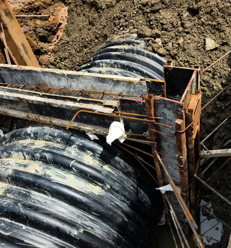 Black corrugated drainage pipe in excavated trench with shoring supports and surrounding soil