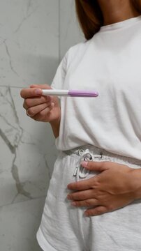 Close-up of woman holding pregnancy test and touching belly, concept of pregnancy planning and reproductive health