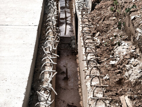Concrete foundation trench with exposed rebar and compacted soil