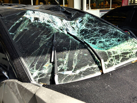 Damaged car windshield and hood with shattered glass and bent trim after impact