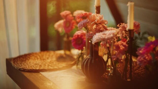 Warm sunset light illuminating flowers in small vases and lit candles on a table in a room