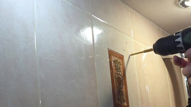 Handheld drill boring into tiled bathroom wall. Home improvement and DIY repair. Renovation, maintenance and household construction