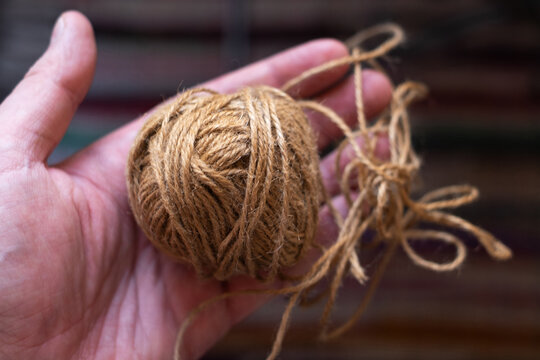 Hand holding ball of natural jute twine with loose loops, brown hemp string skein, rustic craft and eco packaging material