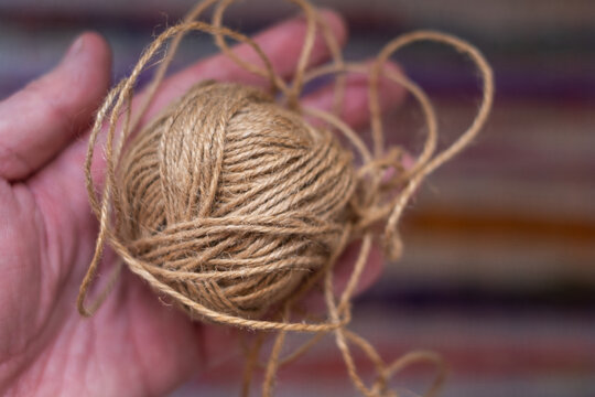 Hand holding ball of natural jute twine with loose loops, brown hemp string skein, rustic craft and eco packaging material