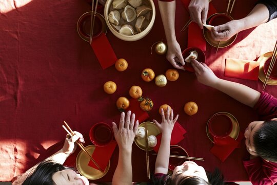Overhead view of multi-generational family sharing dumplings and mandarin oranges at a red table during Lunar New Year celebration