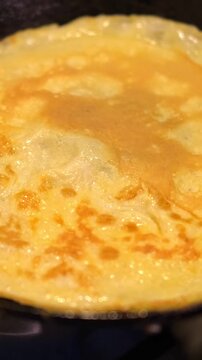 Chef cooking tasty scrambled eggs on kitchen. Homemade Omelette. Fried eggs in a black skillet. Top view. Golden sauteed eggs on the frying pan. Modern cuisine. Preparing breakfast. Cooking at home