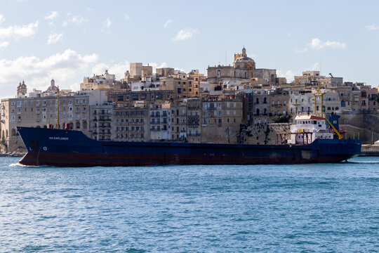 Valletta, Malta - October 14th, 2026 Cargo Ship in Harbor Passing Historic Old Town Waterfront Under Clear Blue Sky