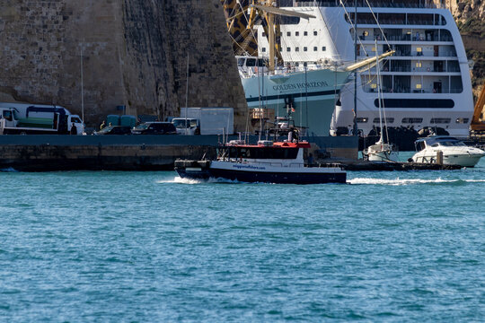 Valletta, Malta - October 14th, 2026 Small Harbor Boat Passing a Cruise Ship Beside a Stone Fort Wall in Sunny Coastal Port