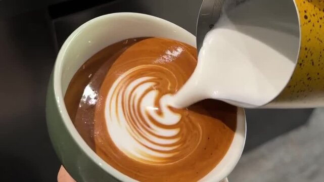 Barista pouring milk to create rosetta and tulip latte art in a green ceramic cup