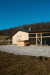 A modern wooden chicken coop with wire mesh pens behind a wooden fence in the foreground on a sunny day. © Аліна Костюк