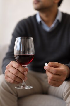 Person holding a glass of red wine and a pill. Antidepressants and alcohol use disorder. Medication interaction and addiction recovery. Mental health treatment and substance misuse awareness
