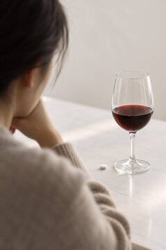 Glass of red wine and a tablet on table beside a seated person. Alcohol use with antidepressant medication. Prescription drug interaction and substance misuse awareness. Mental health care