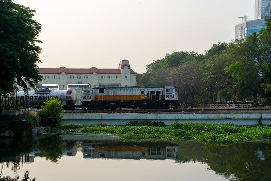 Surabaya, Indonesia - September 09, 2026: PT KAI freight train hauled by a CC 206 locomotive passing near historic Pintu Air Jagir dam reflecting in river water.