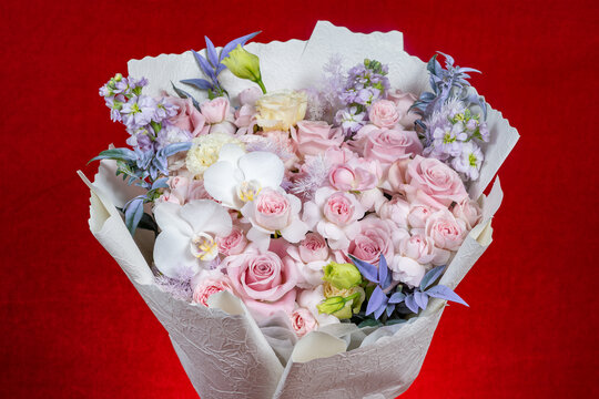 A delicate mixed flower bouquet wrapped with textured white paper against red backdrop