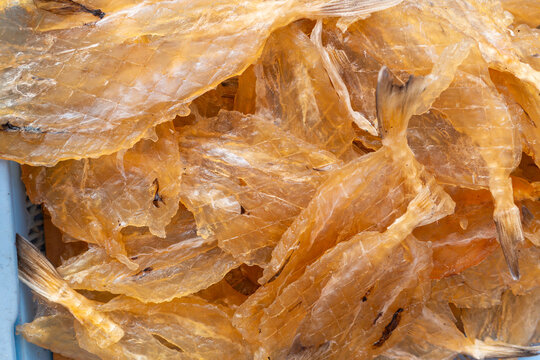 Pile of translucent golden dried fish fillets stacked inside plastic container