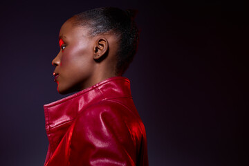 Profile portrait of a dark skinned African woman wearing a red leather jacket against a dark background. Concept of fashion, beauty, confidence, and elegant style in studio lighting. © SHOTPRIME STUDIO