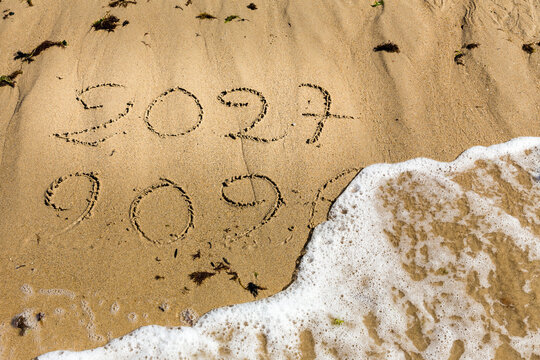 Bonne et heureuse ann&eacute;e 2027, &eacute;l&eacute;gante carte de voeu montrant la fin de 2026 et le passage &agrave; 2027 sur le sable d'une plage.