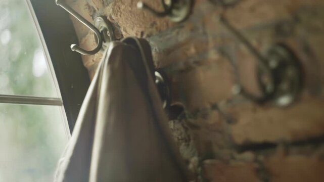Hand hanging clothes metal hook brick wall close up. Old rustic interior window.