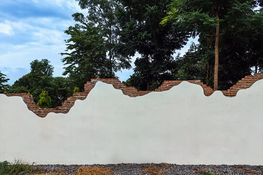 Decorative curved fence wall. Beautiful stuccoed brick wall features unique and attractive design, characterized by uneven, varying height levels. rendered brick wall design non uniform wall heights.