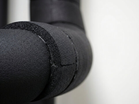 Close-up view of black elastomeric foam pipe insulation installed on a commercial HVAC cooling system chiller line, showing textured rubber material, glued joints, and energy-saving thermal