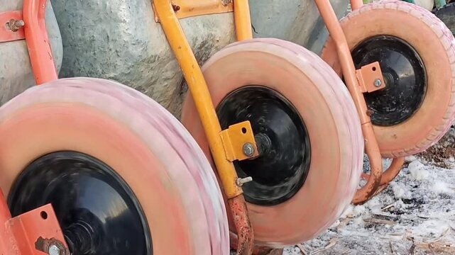 Close-up of construction wheelbarrow wheels spinning. The rotating wheels highlight the details of the tire, axle, and metal frame, capturing movement and construction equipment in action.