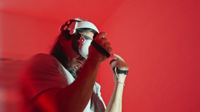Man wearing virtual reality headset executing boxing motions with handheld controllers in red lit room low-angle closeup, immersive training session showing dynamic movement and focused posture, close