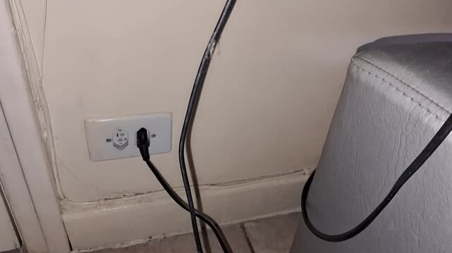 Black power cord plugged into electrical wall socket indoors