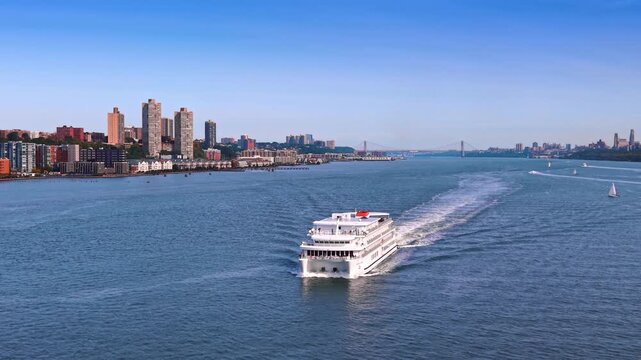 Gorgeous modern white cruise boat approaches by the riverscape. Sone sailboats on the waterscape in the backdrop. New York City, USA at daytime.