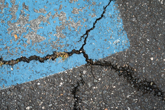 visible cracks in the asphalt blacktop surface of a car parking lot with faded blue paint from a handicap accessible space painted on to the paved roadway