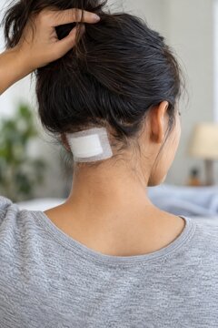 Woman lifting hair to reveal adhesive bandage on back of neck at home