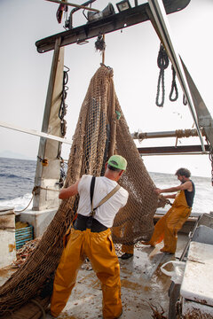 Fishermen guiding a heavy trawl net on deck