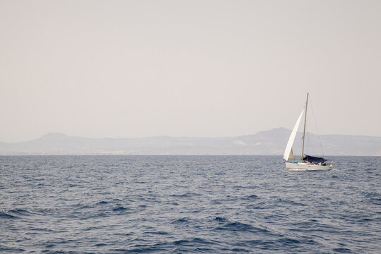 Sailboat crossing open sea with distant coastline
