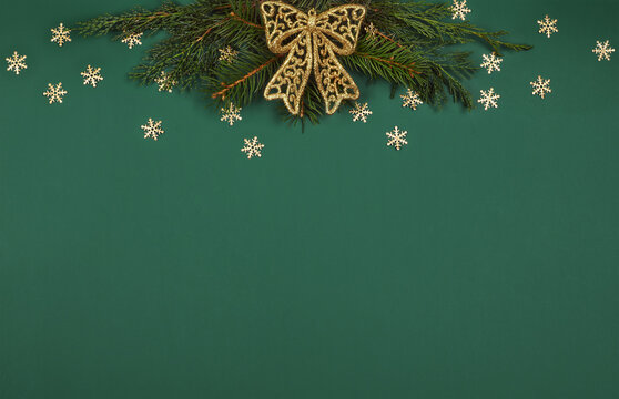 Christmas golden decorations and pine twigs in top border on green paper background.