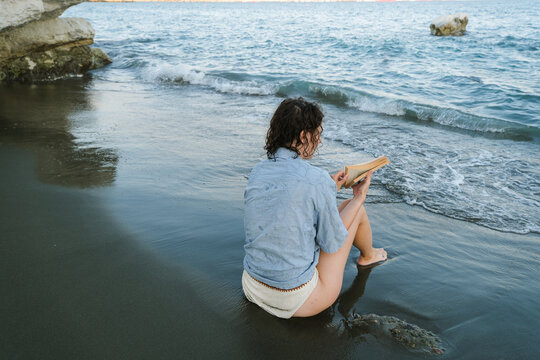 Person Sitting on the Beach and Writing in a Notebook by the Water