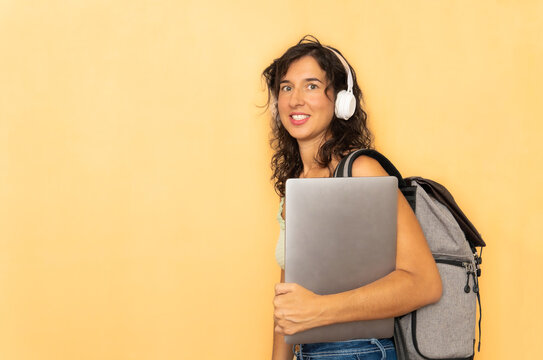 Female student with backpack and headphones holding laptop