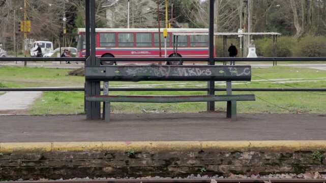 Empty Bench on Train Station Platform with City Bus Passing in Background in Buenos Aires Province, Argentina 