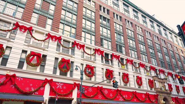 Brick stories rise above Christmas wreaths at Herald Square. A low angle shows cream masonry and red garland panels beneath rows of windows.