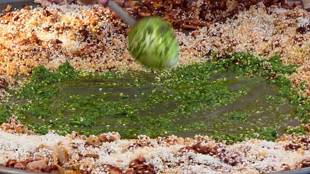 Chef adding fresh green herb and garlic sauce to a large traditional seafood paella during a street food culinary festival in Spain.