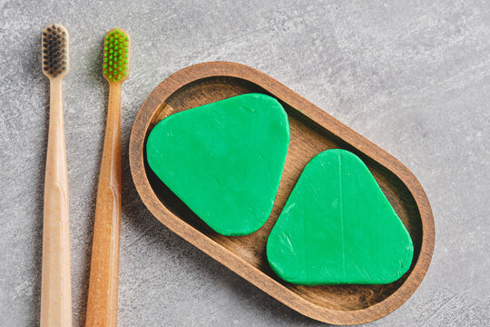 Two bamboo toothbrushes and solid shampoo bars inside wooden dish on gray countertop.