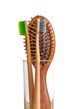 Close up eco toothbrushes and wooden hairbrush in glass cup against white background.