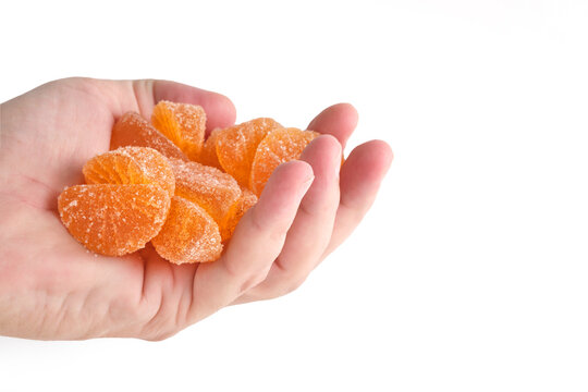 Male hand holding handful orange citrus marmalade candies coated in sugar over white background.