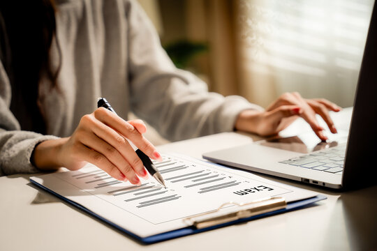 Online education concept. Close-up of a woman completing an exam on a clipboard while using a laptop at a desk indoors in natural light. Exam, education, assessment, learning, testing.