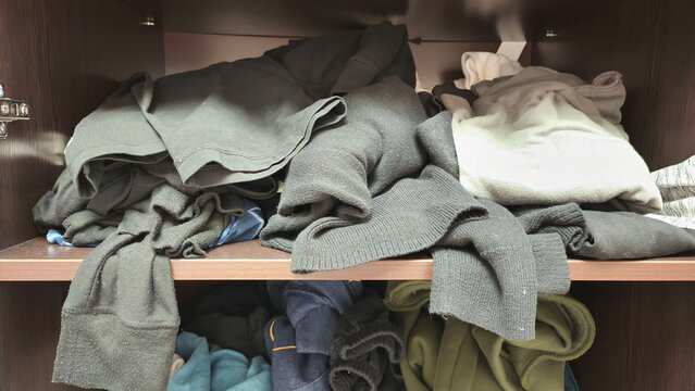 Pile of messy clothes on a closet shelf at home, illustrating wardrobe clutter, laundry overload, storage organization, decluttering, and everyday household life.
