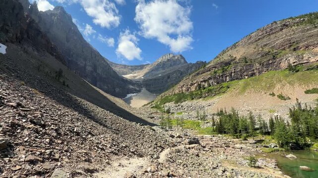 POV walking on rocky trail along Lake Agnes shore, then camera pans to emerald water below Big Beehive slope in Banff, Alberta. Concept of alpine hiking tourism and mountain freshwater conservation.