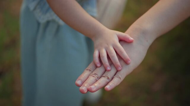 Close up of little child's hand gently resting on mother's hand outdoors, tender moment of physical connection expressing love, trust and family bonding, parenting care